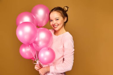 Beyaz şirin giysiler içindeki genç kız heyecanlı. Kadın model altın arka plan üzerinde pembe hava balonları ile. St. kadınlar günü; Mutlu yeni yıl; Doğum günü tatil partisi