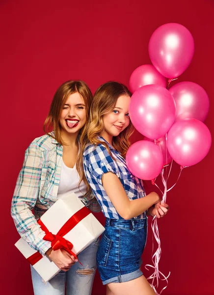 两个面带微笑的美女穿着格子衬衫的衣服 女孩在红色背景摆姿势 带有大礼品盒和粉红色气球的模型 玩得开心 准备庆祝新年 — 图库照片