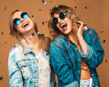İki genç güzel gülümseyen hippi kız trendy yaz giysileri ve güneş gözlüğü. Altın arka plan üzerinde poz seksi kaygısız kadın. Konfeti altında pozitif çığlık modelleri.