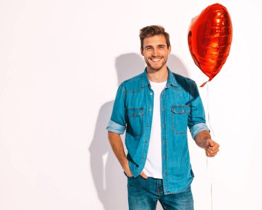 Portre yakışıklı gülümseyen şık hipster lumbersexual modeli kot elbise giymiş. Kalp tutan moda adam hava balonu şeklinde. Beyaz izole