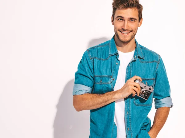 Portrait of handsome smiling man wearing summer hipster jeans clothes. Model male holding vintage photo camera. Isolated on white