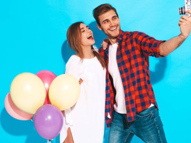 Gülen Güzel Kız ve onun Yakışıklı Erkek arkadaşı renkli hava balonları demet tutan. Mutlu Aile kendi fotoğraflarını çekiyor. Aşk. Sevgililer günün kutlu olsun. Mavi duvarın yakınında poz vermek