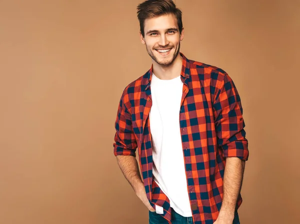 Portrait of handsome smiling stylish hipster lumbersexual businessman model dressed red checkered shirt. Fashion man. Posing on golden background