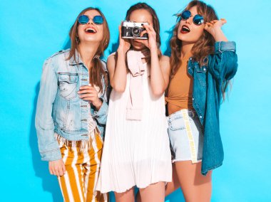 Üç genç güzel gülümseyen hippi kız trendy yaz rahat kıyafetler ve güneş gözlüğü. Seksi kaygısız kadın mavi duvara yakın poz. Retro kamera resim çekme