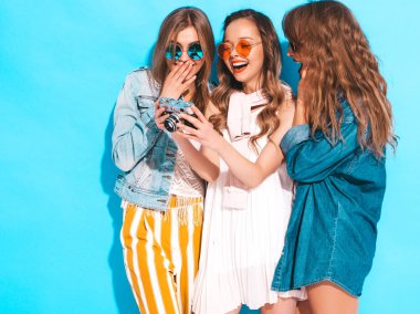 Üç genç güzel gülümseyen hippi kız trendy yaz rahat kıyafetler ve güneş gözlüğü. Seksi kaygısız kadın mavi duvara yakın poz. Retro kamera resim çekme