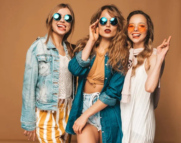 三个美丽的微笑的嬉皮士女孩在时尚夏季休闲服和太阳镜 性感无忧无虑的女人摆在金色的墙附近 积极的模特疯了显示和平的迹象和舌头 — 图库照片