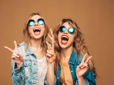 İki genç güzel gülümseyen hippi kız trendy yaz kot giyim ve güneş gözlüğü. Seksi kaygısız kadın Studio altın arka plan üzerinde poz. Pozitif çığlık gösteren barış işareti modelleri