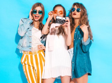 Üç genç güzel gülümseyen hippi kız trendy yaz renkli elbise ve güneş gözlüğü. Seksi kaygısız kadın mavi duvara yakın poz. Retro kamera resim çekme