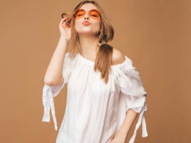Güzel gülümseyen şirin model pembe dudakları ile portresi. Yaz beyaz hipster elbiseli kız. Model altın arka planda güneş gözlüğü üzerinde poz