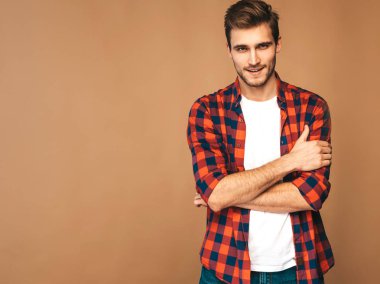 Portrait of handsome smiling stylish hipster lumbersexual businessman model dressed in red checkered shirt. Fashion man posing on golden background. Crossed arms clipart