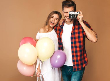 Gülümseyen güzel kız ve yakışıklı renkli hava balonları demet tutan erkek arkadaşı. Mutlu aile alarak resmi retro kamera için kendilerini. Sevgililer günün kutlu olsun. Altın duvara yakın poz