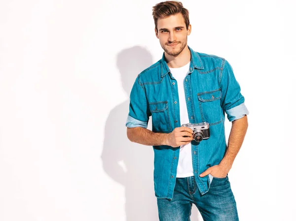 Portrait of handsome smiling man wearing summer hipster jeans clothes. Model male taking picture on old vintage photo camera. Isolated on white