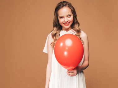 Genç kız trendy yaz beyaz elbisenin içinde poz heyecanlı. Kadın model altın arka plan üzerinde poz kırmızı hava balonu ile. Parti için hazır