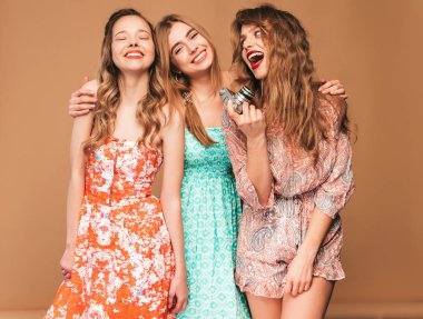 Üç genç güzel gülümseyen hippi kız trendy yaz casual elbiseler. Seksi kaygısız kadın altın duvara yakın poz. Retro kamera resim çekme