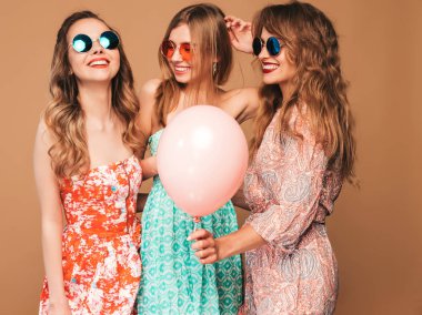 Kareli gömlekli üç gülümseyen güzel kadın kıyafetleri yaz. Altın arka plan üzerinde poz kızlar. Renkli balonlar içinde güneş gözlüğü modelleri. Eğleniyor, kutlama Doğum günü veya tatil parti için hazır