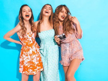 Üç genç güzel gülümseyen hippi kız trendy yaz casual elbiseler. Seksi kaygısız kadın mavi duvara yakın poz. Retro kamera resim çekme
