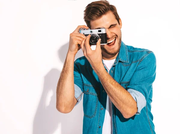 Portrait of handsome smiling man wearing summer hipster jeans clothes. Model male taking picture on old vintage photo camera. Isolated on white