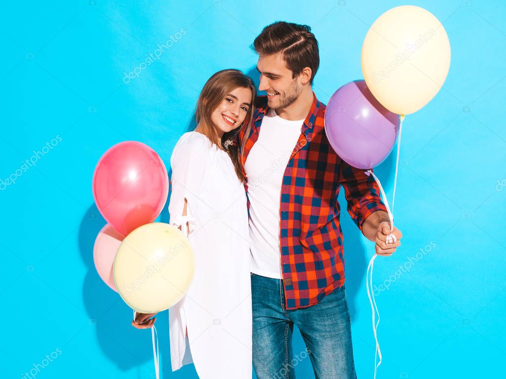 Portrait of Smiling Beautiful Girl and her Handsome Boyfriend holding bunch of colorful air balloons and laughing. Happy Family. Love. Happy Valentine's Day. Isolated on blue wall