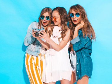 Üç genç güzel gülümseyen hippi kız trendy yaz casual elbise ve güneş gözlüğü. Seksi kaygısız kadın mavi duvara yakın poz. Retro kamera resim çekme