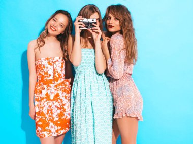 Üç genç güzel gülümseyen hippi kız trendy yaz casual elbiseler. Seksi kaygısız kadın mavi duvara yakın poz. Retro kamera resim çekme