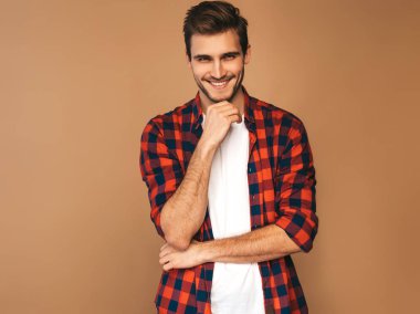 Portre yakışıklı gülümseyen şık hipster lumbersexual işadamı model kırmızı kareli gömlek giymiş. Altın arka plan üzerinde poz moda adam. Çenesine dokunuyor