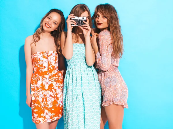 Üç genç güzel gülümseyen hippi kız trendy yaz casual elbiseler. Seksi kaygısız kadın mavi duvara yakın poz. Retro kamera resim çekme