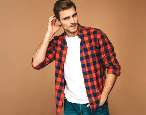 Portrait of handsome smiling stylish hipster lumbersexual businessman model dressed in red checkered shirt. Fashion man posing on golden background