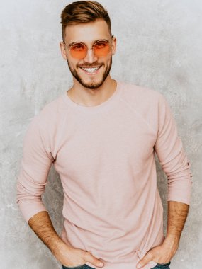 Portre yakışıklı gülümseyen hipster lumbersexual işadamı modeli rahat yaz pembe elbise giyiyor. Moda şık adam yuvarlak güneş gözlüğü gri duvara poz