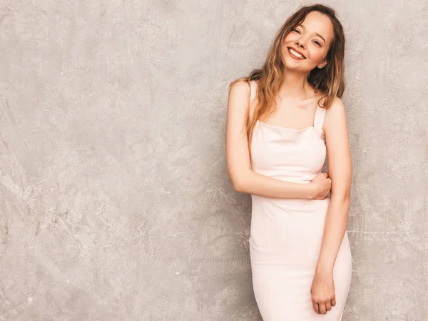 Trendy yaz hafif pembe elbiseli genç güzel gülümseyen hipster kız portresi. Seksi kaygısız kadın gri duvara yakın poz. Olumlu model eğleniyor