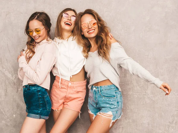 Üç genç güzel gülümseyen hippi kız trendy yaz spor giysileri. Seksi kaygısız kadın gri duvara yakın poz. Olumlu modelleri yuvarlak güneş gözlüğü eğleniyor. Sarılma