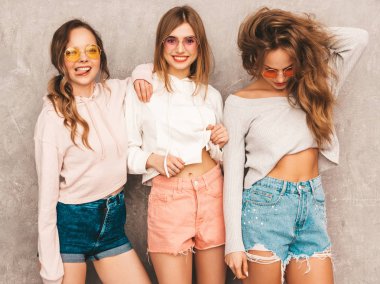 Üç genç güzel gülümseyen hippi kız trendy yaz spor giysileri. Seksi kaygısız kadın gri duvara yakın poz. Olumlu modelleri yuvarlak güneş gözlüğü eğleniyor. Sarılma