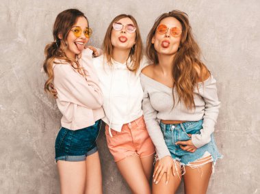 Üç genç güzel gülümseyen hippi kız trendy yaz spor giysileri. Seksi kaygısız kadın gri duvara yakın poz. Olumlu modelleri yuvarlak güneş gözlüğü eğleniyor. Onların dilini gösterilen