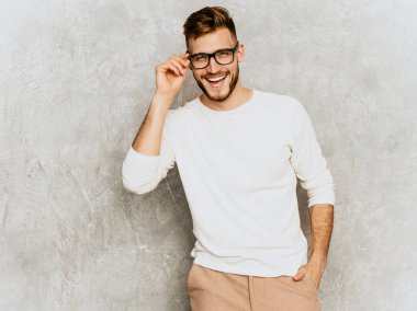 Portre yakışıklı gülümseyen hipster lumbersexual işadamı modeli giyiyor rahat yazlık beyaz giysiler ve gözlük. Moda şık adam gri duvara poz