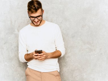 Yakışıklı gülümseyen hipster lumbersexual işadamı modeli rahat yaz beyaz elbise giyen portresi. Moda şık adam gri duvara poz. Cep telefonunuzla gözlükler