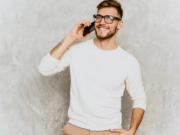 帅气的微笑的嬉皮士伐木工人的肖像伐木业商人穿着休闲的夏季白色服装 时尚时尚的男人摆出对灰色的墙壁 用眼镜在手机上讲话 — 图库照片