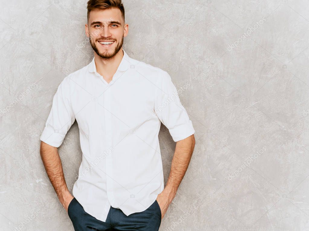 Portrait of handsome smiling hipster lumbersexual businessman model wearing casual summer white shirt. Fashion stylish man posing against gray wall