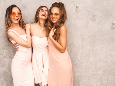 Üç genç güzel gülümseyen hippi kız trendy yaz ışık elbiseler pembe. Seksi kaygısız kadın gri duvara yakın poz. Pozitif eğleniyor yuvarlak güneş gözlüğü modellerinde