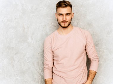 Yakışıklı emin hipster lumbersexual işadamı modeli giyiyor rahat yazlık pembe giysiler portresi. Moda şık adam gri duvara poz. Gün ışığı