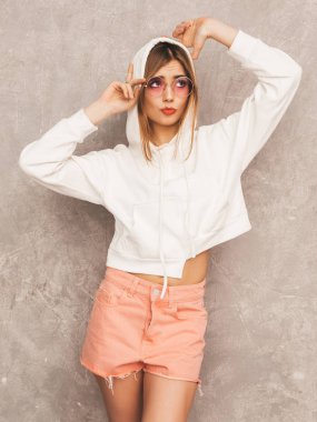 Trendy yaz hipster spor giysileri güzel genç gülümseyen kız portresi. Seksi kaygısız kadın gri duvara yakın poz. Olumlu model içinde güneş gözlüğü eğleniyor