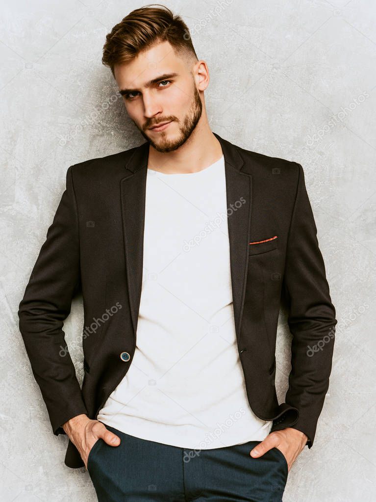 Portrait of handsome serious hipster lumbersexual businessman model wearing casual black suit. Fashion stylish man posing against gray wall