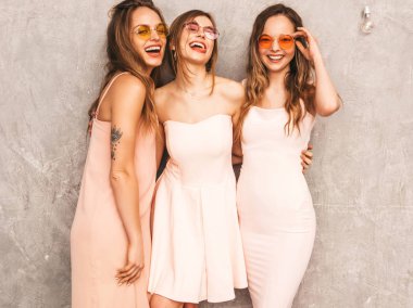 Üç genç güzel gülümseyen hippi kız trendy yaz ışık elbiseler pembe. Seksi kaygısız kadın gri duvara yakın poz. Pozitif eğleniyor yuvarlak güneş gözlüğü modellerinde