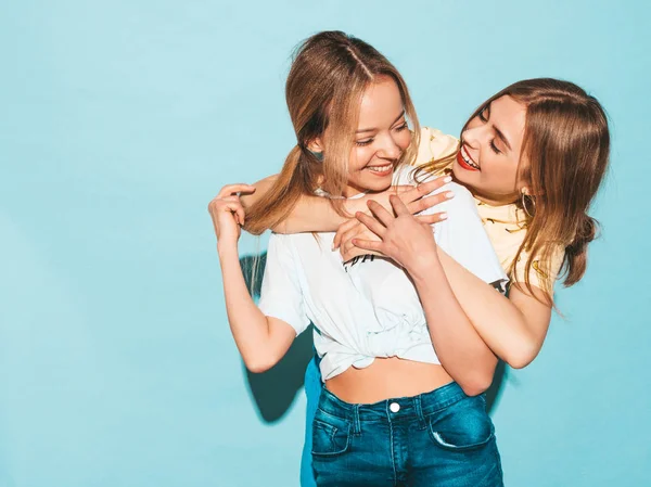两个年轻美丽的微笑的金发嬉皮士女孩在时尚夏天五颜六色的 T恤衣服 性感无忧无虑的妇女摆姿势附近的蓝色墙壁 积极的模型有乐趣和拥抱 — 图库照片