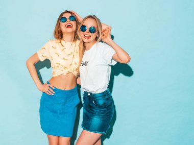 İki genç sarışın hippi kız trendy yaz Jeans gülümseyen güzel elbise etek. Seksi kaygısız kadın yuvarlak güneş gözlüğü mavi duvarının yakınında poz. Eğleniyor ve sarılma olumlu modelleri