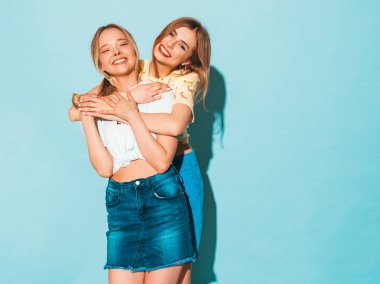 İki genç trendy sarışın hipster kızlarda gülümseyen güzel renkli tişört elbise yaz. Seksi kaygısız kadın mavi duvara yakın poz. Eğleniyor ve sarılma olumlu modelleri