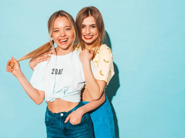 两个年轻美丽的微笑的金发嬉皮士女孩在时尚夏天五颜六色的 T恤衣服 性感无忧无虑的女人摆在蓝色的墙壁附近 积极的模型有乐趣和拥抱 — 图库照片