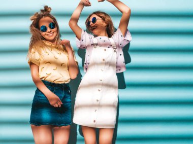 İki genç trendy sarışın hipster kızlarda gülümseyen güzel renkli tişört elbise yaz. Yuvarlak güneş gözlüğü mavi duvarının yakınında dans seksi kaygısız kadın. Olumlu modelleri eğleniyor