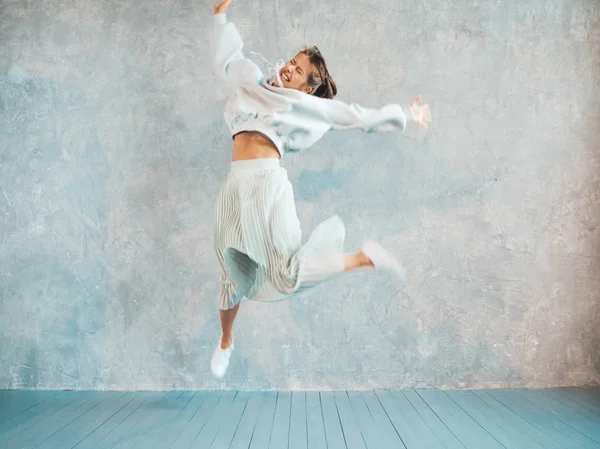 Beautiful cute smiling model jumping. Girl in summer hipster hoodie and skirt. Model having fun and going crazy near gray wall in studio