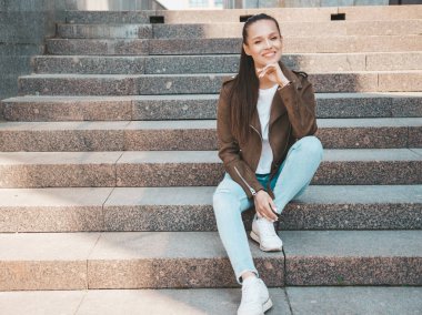 Yaz hipster ceket ve kot elbise giymiş güzel gülümseyen esmer model Portresi. Sokak arka planda merdivenlerde oturan trendy kız. Komik ve pozitif kadın 