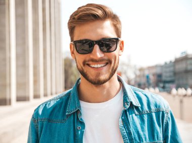 Yakışıklı gülümseyen şık hipster lumbersexual işadamı modeli portresi. Kot pantolon ceketi giymiş bir adam. Moda erkek güneş gözlüğü sokak arka planda poz