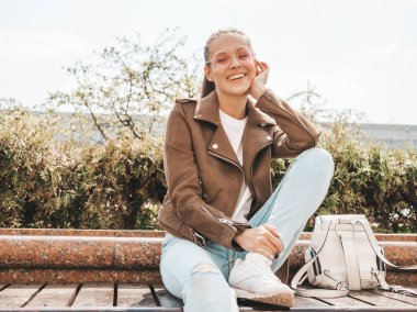 Yaz hipster ceket ve kot elbise giymiş güzel gülümseyen esmer model Portresi. Sokak arka planda bankta oturan trendy kız. Güneş gözlüğü komik ve pozitif kadın
